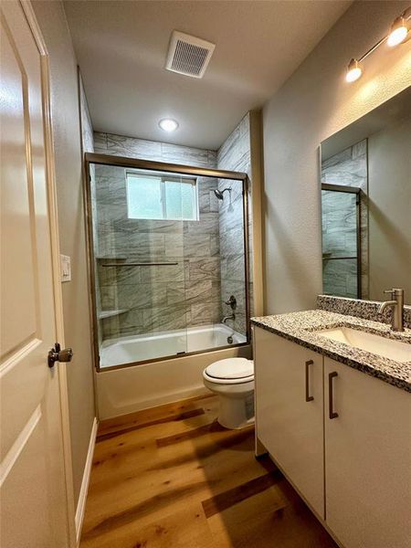 Full bathroom featuring shower / bath combination with glass door, vanity, hardwood / wood-style flooring, and toilet