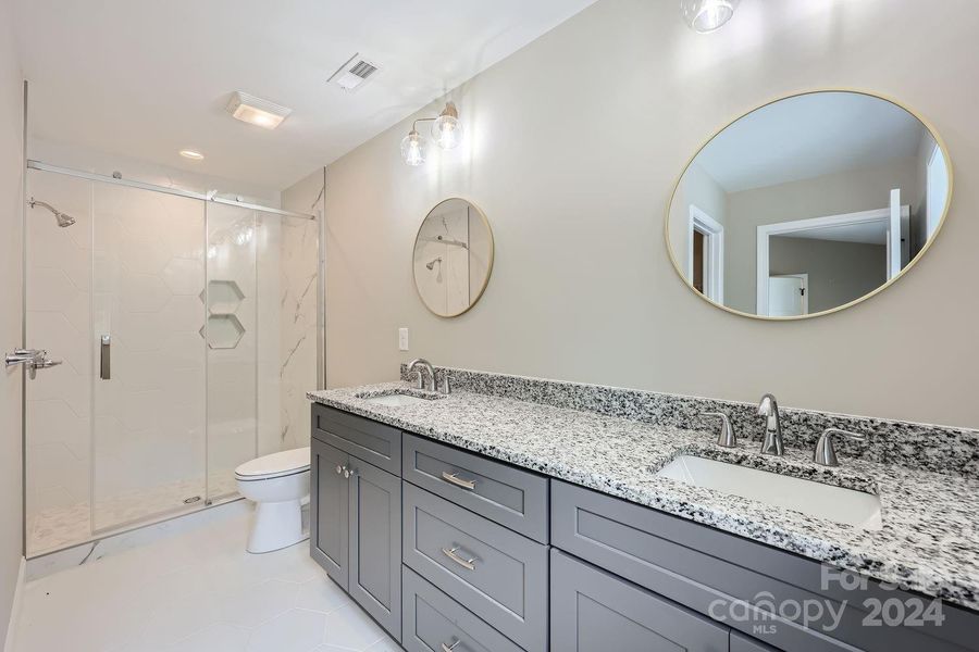 Primary suite bathroom with granite double vanity and sizable walk in shower.