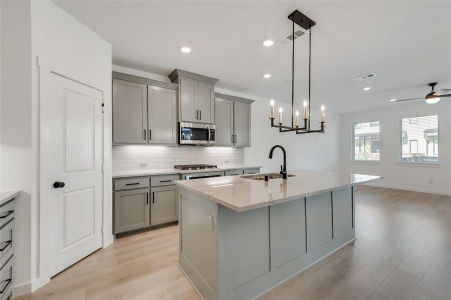 Kitchen featuring ceiling fan with notable chandelier, light hardwood / wood-style floors, hanging light fixtures, decorative backsplash, and sink