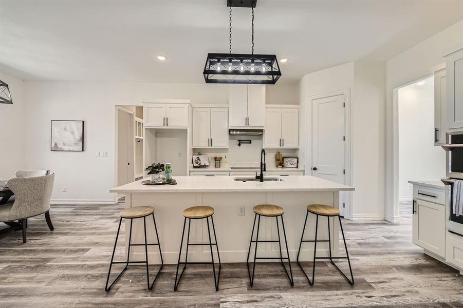 Kitchen featuring a breakfast bar, white cabinets, a kitchen island with sink, and sink