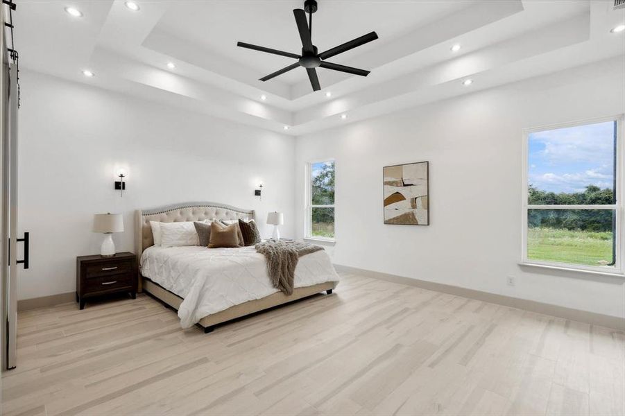 Bedroom with light hardwood / wood-style floors, ceiling fan, and a tray ceiling