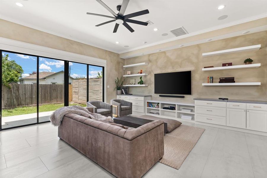 The living room boasts built-in cabinets and floating shelves, tile flooring, and a large glass sliding door that fills the space with natural light and provides easy access to the outdoors.