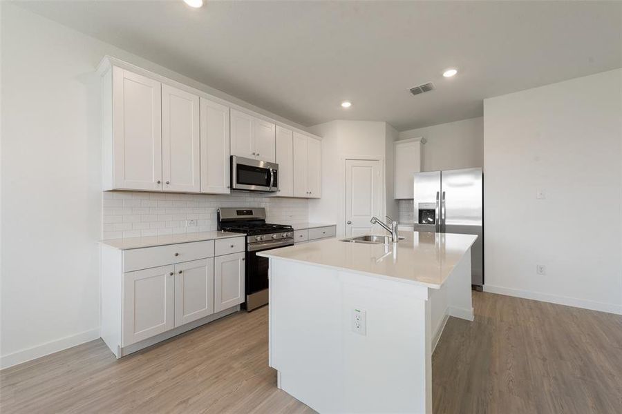 Kitchen featuring white cabinets, an island with sink, stainless steel appliances, and light wood-type flooring