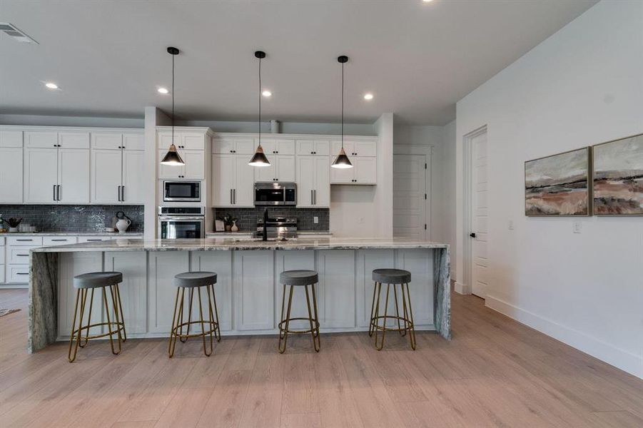 Kitchen featuring tasteful backsplash, stainless steel appliances, white cabinets, light hardwood / wood-style floors, and a large island with sink