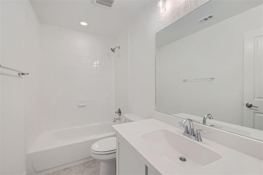 Full bathroom with tiled shower / bath, vanity, tile patterned flooring, and toilet