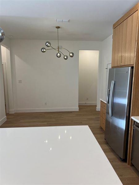 Kitchen with stainless steel appliances, hanging light fixtures, a chandelier, dark hardwood / wood-style floors, and light brown cabinetry