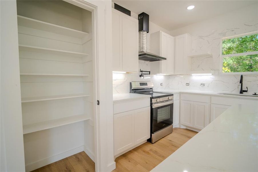 Kitchen with light stone countertops, sink, white cabinets, and stainless steel range oven