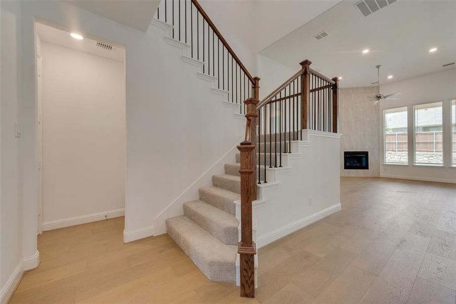 Stairs with a tile fireplace, light wood-type flooring, and ceiling fan