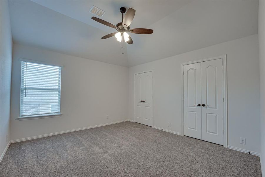 Unfurnished bedroom featuring carpet floors, ceiling fan, vaulted ceiling, and two closets