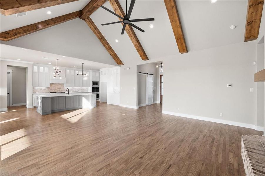 Unfurnished living room with light hardwood / wood-style floors, beam ceiling, a barn door, and high vaulted ceiling