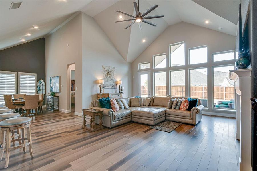 Living room with high vaulted ceiling, ceiling fan, a stone fireplace, and hardwood floors.