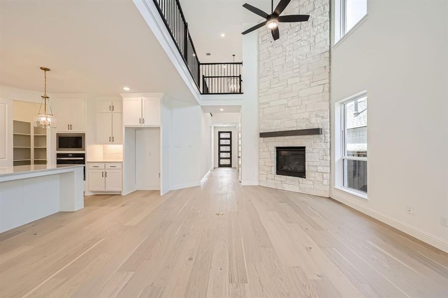 Unfurnished living room with a stone fireplace, light hardwood / wood-style floors, ceiling fan with notable chandelier, and a high ceiling