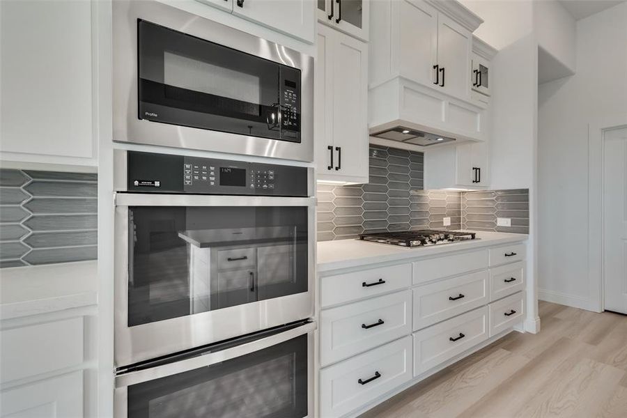 Kitchen with stainless steel appliances, light hardwood / wood-style floors, white cabinets, and tasteful backsplash