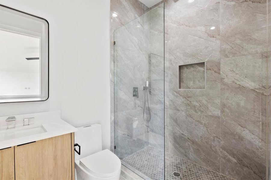 Bathroom featuring a tile shower, vanity, and toilet