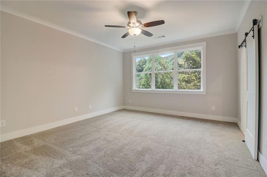 Empty room with a barn door, ceiling fan, ornamental molding, and light colored carpet