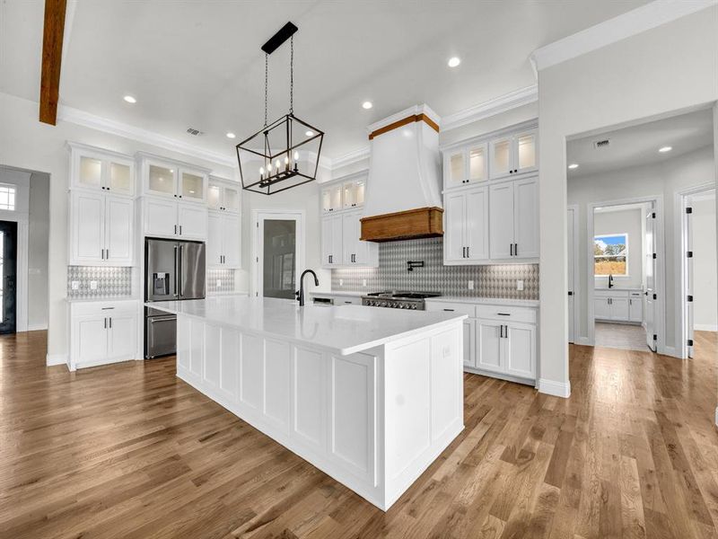 Kitchen with white cabinets, a kitchen island with sink, stainless steel appliances, and custom range hood