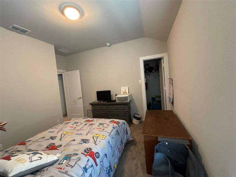 Bedroom with lofted ceiling, a spacious closet, dark colored carpet, and a closet