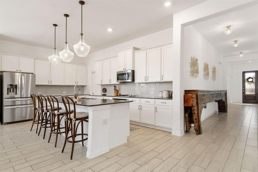 Kitchen with appliances with stainless steel finishes, hanging light fixtures, white cabinetry, decorative backsplash, and a center island with sink