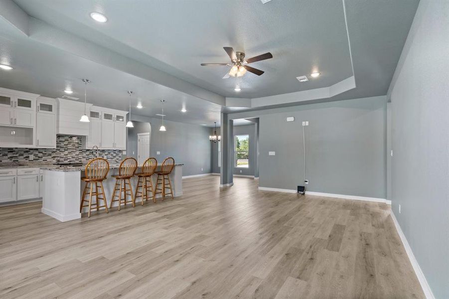 Unfurnished living room featuring a tray ceiling, ceiling fan, indoor bar, and light hardwood / wood-style flooring