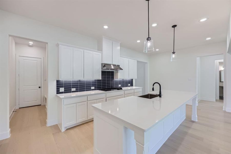 Kitchen featuring white cabinetry, hanging light fixtures, sink, and a center island with sink