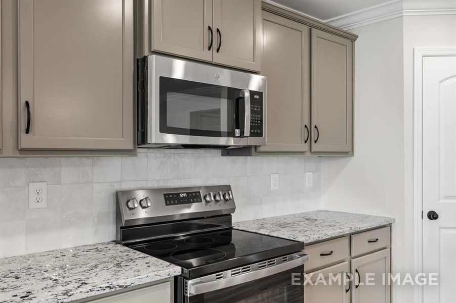 Kitchen with gray cabinetry, crown molding, appliances with stainless steel finishes, light stone countertops, and decorative backsplash