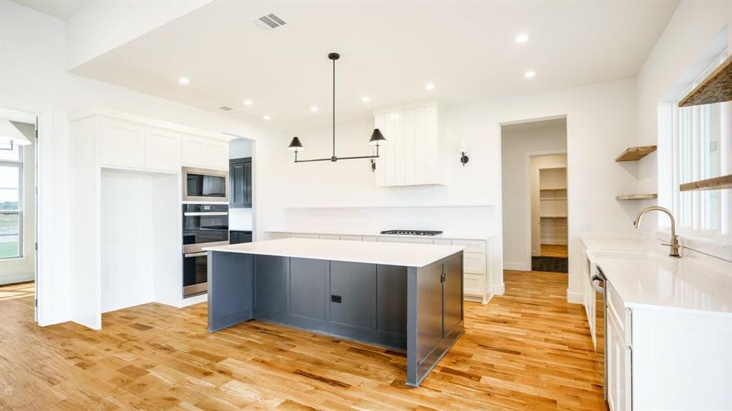 Kitchen with white cabinets, hanging light fixtures, a center island, light wood-type flooring, and black microwave