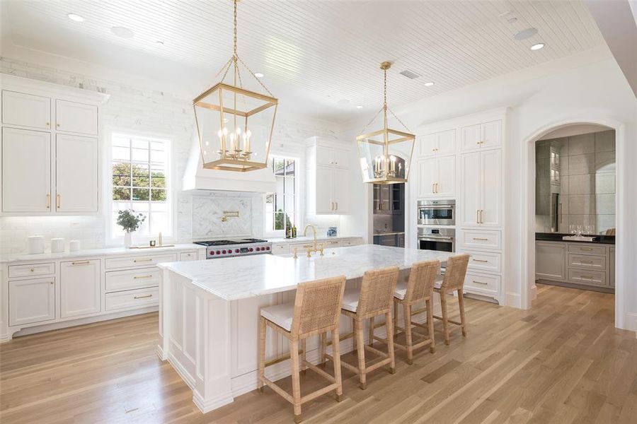 Kitchen featuring light wood flooring, tasteful backsplash, white cabinets, and a center island with sink