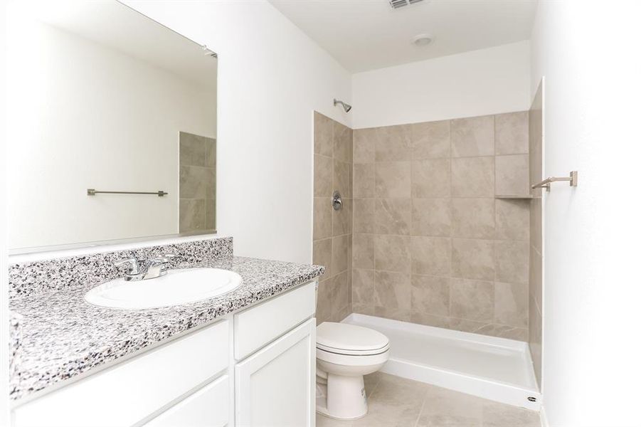 Primary Bathroom featuring a tile shower, tile patterned flooring, vanity, and toilet. Shelving not pictured.