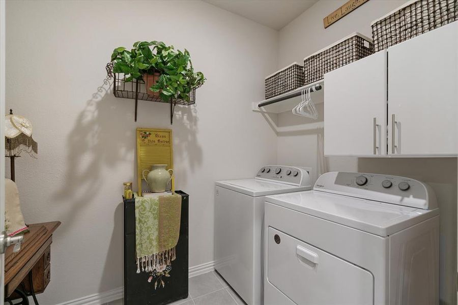 Laundry room off hallway to garage. Washing machine and dryer stay with the home. Storage cabinets, and light tile patterned floors.