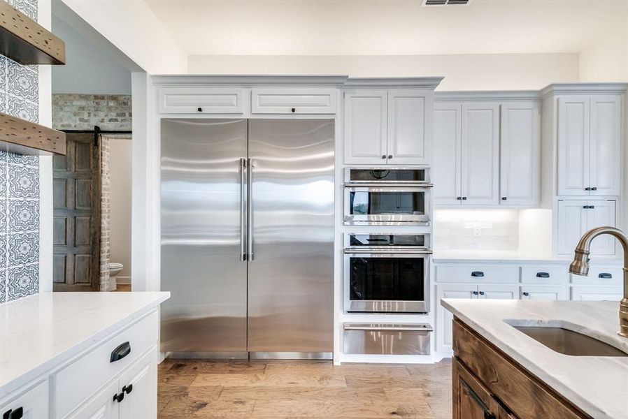 Kitchen with sink, light hardwood / wood-style flooring, backsplash, stainless steel appliances, and a barn door