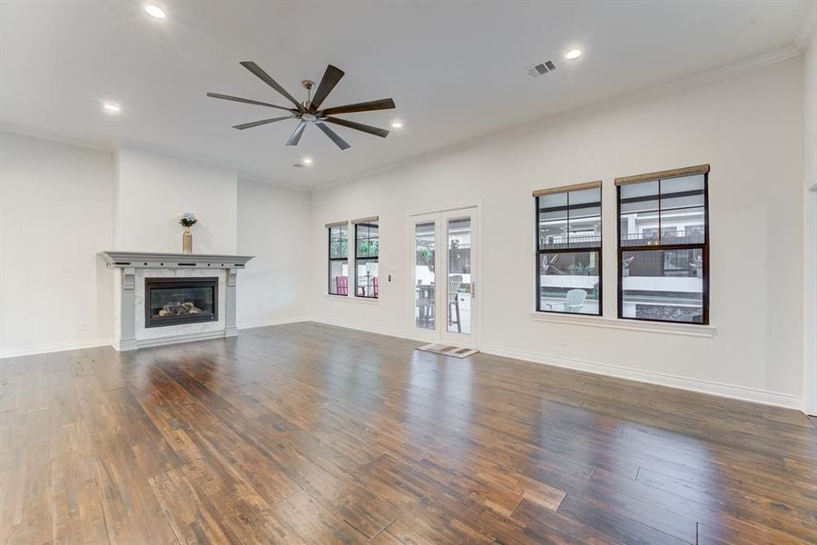 This is a spacious, well-lit living room featuring a cozy fireplace and large windows with a view to the outside. There's also direct access to the back patio area through the French doors.