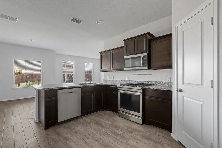 Kitchen with a wealth of natural light, appliances with stainless steel finishes, kitchen peninsula, and light hardwood / wood-style flooring