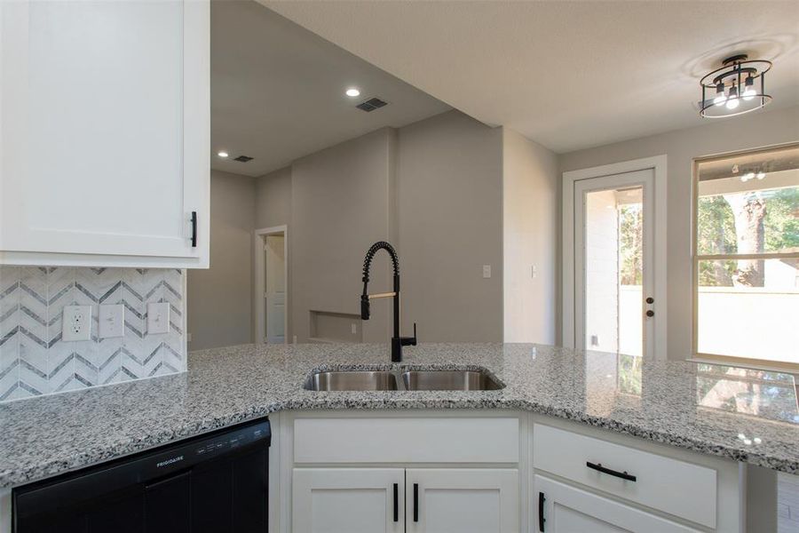 Kitchen featuring dishwasher, light stone counters, sink, white cabinets, and backsplash