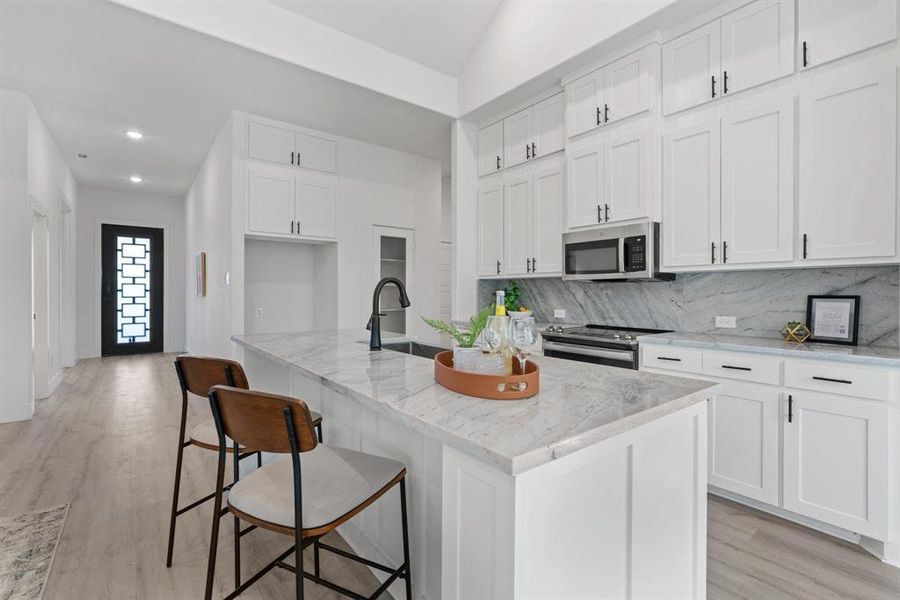 Kitchen with light stone counters, white cabinets, a center island with sink, and stainless steel appliances