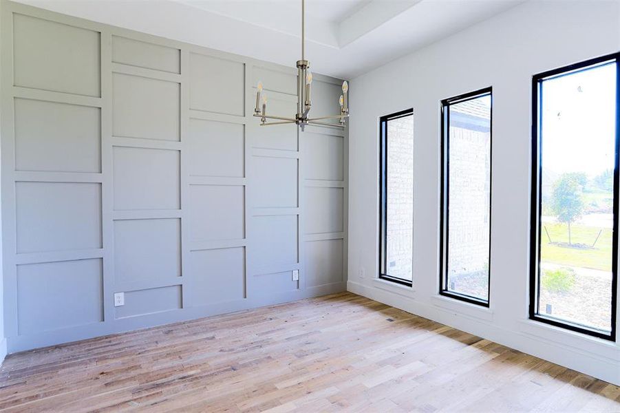 Empty room featuring a chandelier, light wood-type flooring, and a raised ceiling