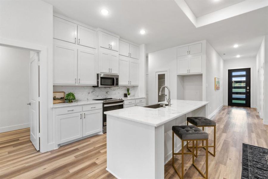 Kitchen with white cabinets, a center island with sink, appliances with stainless steel finishes, and sink