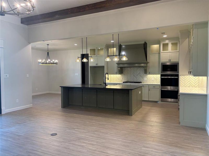 Kitchen featuring pendant lighting, beamed ceiling, a center island with sink, light hardwood / wood-style flooring, and decorative backsplash