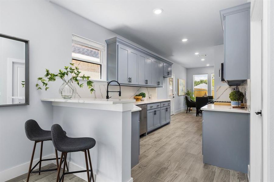 Kitchen with a breakfast bar area, kitchen peninsula, gray cabinetry, decorative backsplash, and light hardwood / wood-style flooring