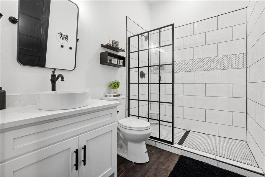 Bathroom with tiled shower, toilet, vanity, and hardwood / wood-style flooring