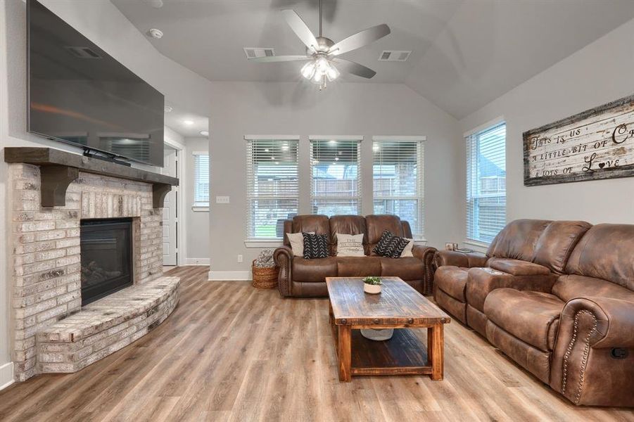 Living room featuring a brick fireplace, light wood-type flooring, vaulted ceiling, and ceiling fan