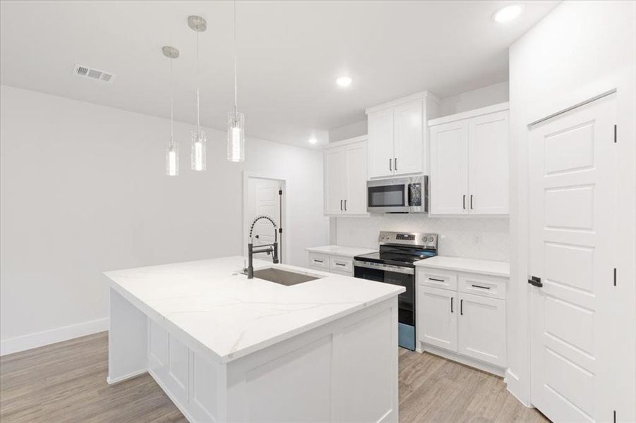 Kitchen with hanging light fixtures, stainless steel appliances, sink, white cabinetry, and light wood-type flooring