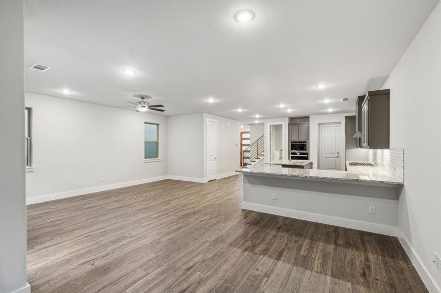 Kitchen featuring hardwood / wood-style floors, a breakfast bar, kitchen peninsula, light stone countertops, and ceiling fan