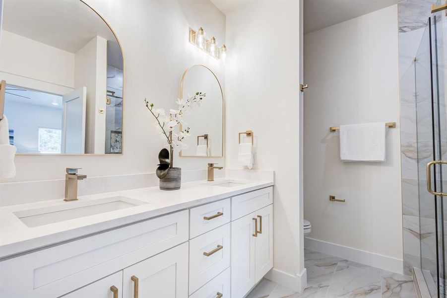 Bathroom featuring tile flooring, double sink, an enclosed shower, vanity with extensive cabinet space, and toilet