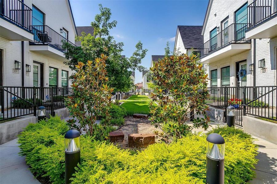The community area is beautifully landscaped, featuring lush greenery, vibrant flower beds, and well-manicured lawns. Paved walkways meander through the space, leading to cozy seating areas and shaded spots perfect for relaxation.