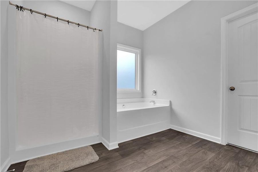 Bathroom with hardwood / wood-style floors, a bath to relax in, and vaulted ceiling