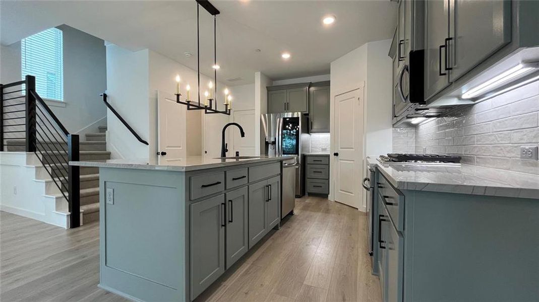 Kitchen featuring sink, pendant lighting, light hardwood / wood-style floors, decorative backsplash, and an island with sink