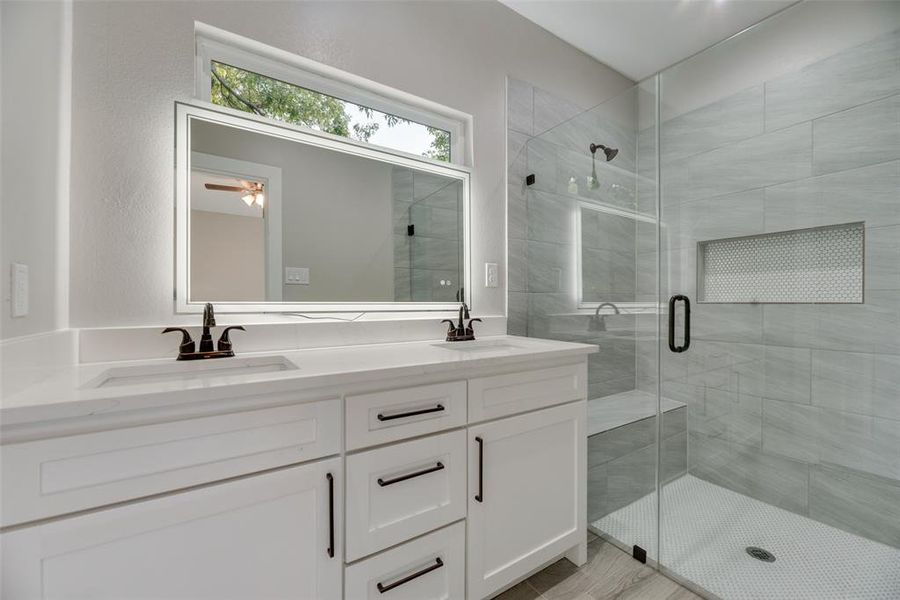 Bathroom featuring dual quartz vanity, a shower with shower door
