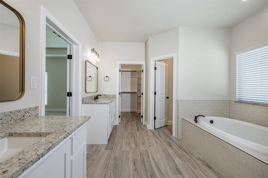 Bathroom featuring vanity, hardwood / wood-style floors, and a relaxing tiled tub