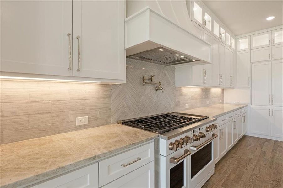 Kitchen with hardwood / wood-style floors, premium range hood, backsplash, gas range, and white cabinetry