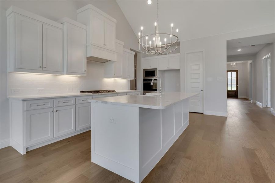 Kitchen with white cabinets, light wood-type flooring, backsplash, and a kitchen island with sink